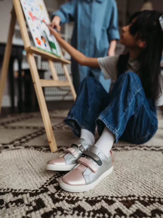 Little girl painting wearing Pip and Henry double Velcro metallic sneakers.