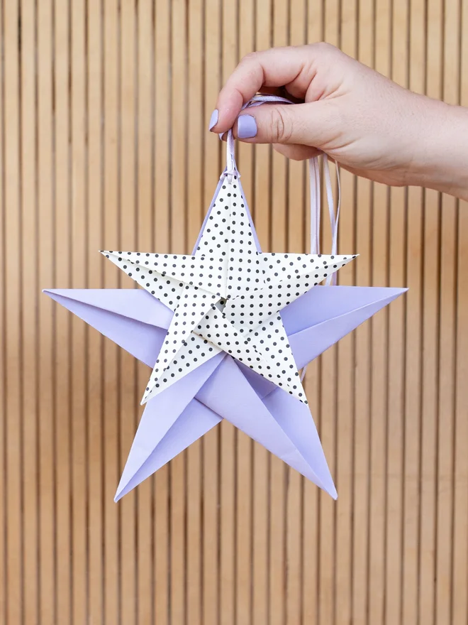 Women holding out 2 origami stars hanging on ribbon