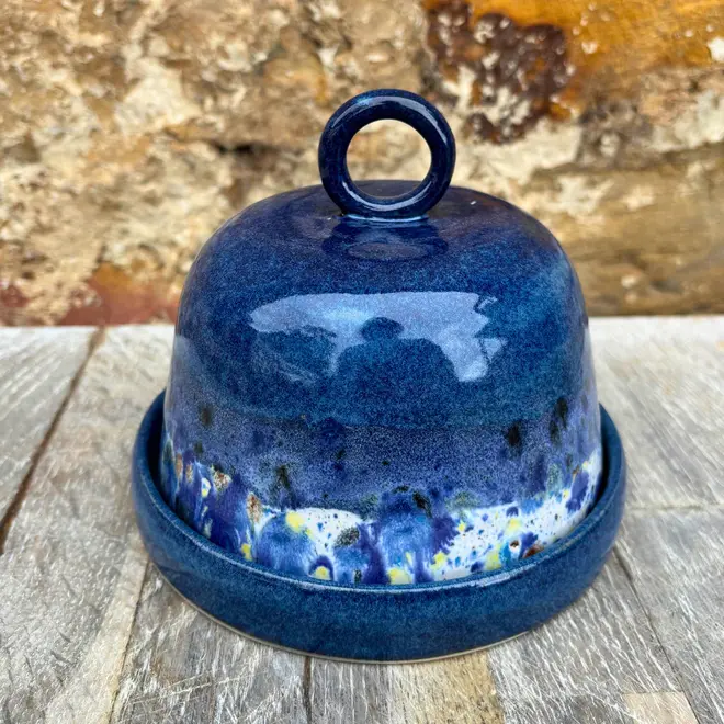 Shoreline Butter Dish, a colourful butter dish placed on a wooden surface against a brick wall. 
