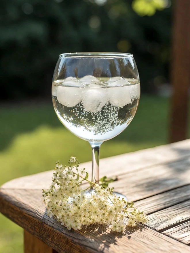 Elderflower Cordial (Set Of 1, 2, 3 Or 4), a glass of cordial sitting on a wooden surface outside. 