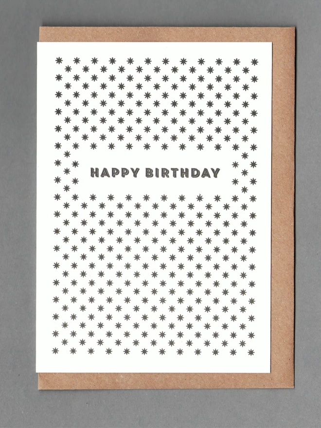 White card with black stars and black text reading 'Happy Birthday' with a kraft envelope behind it