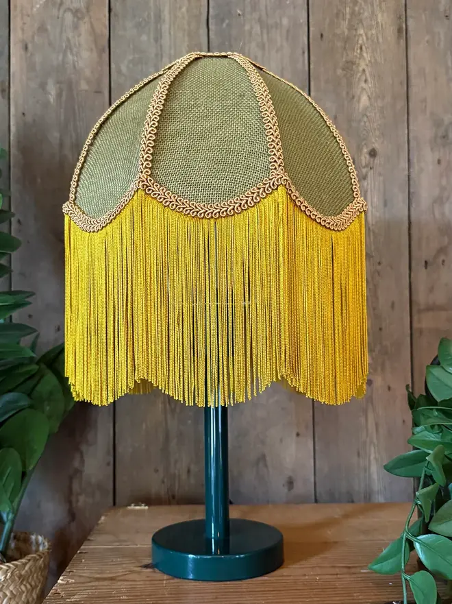 Fringed Hessian Lampshade In Pickle Green And Antique Gold, in a room. 
