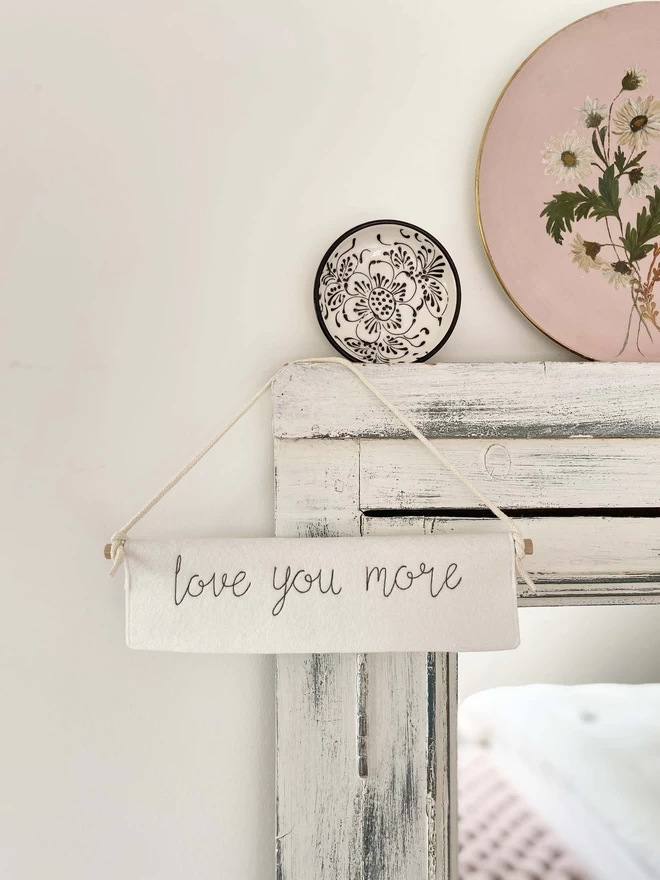 Love You More Felt Embroidered Banner hanging on mirror with plates