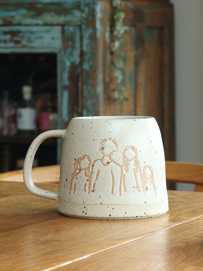 Childrens Drawing Handmade Ceramic Mug on a wooden table. The 'drawing' features a family of four people