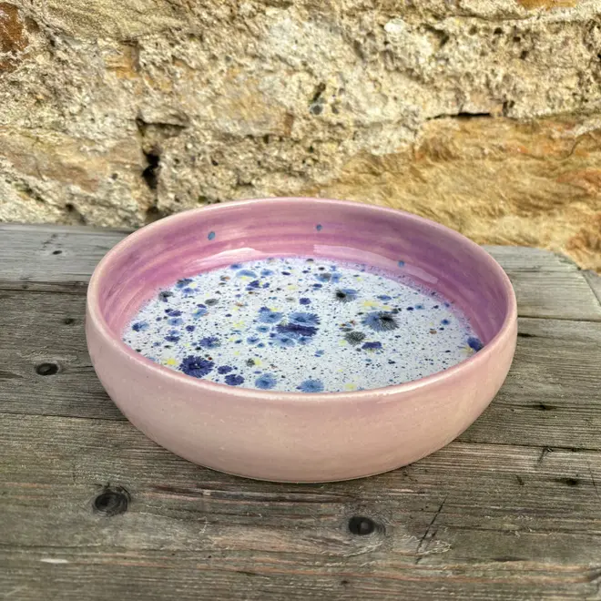 Shoreline Pasta Bowl, a colourful bowl placed on a wooden surface against a brick backdrop. 