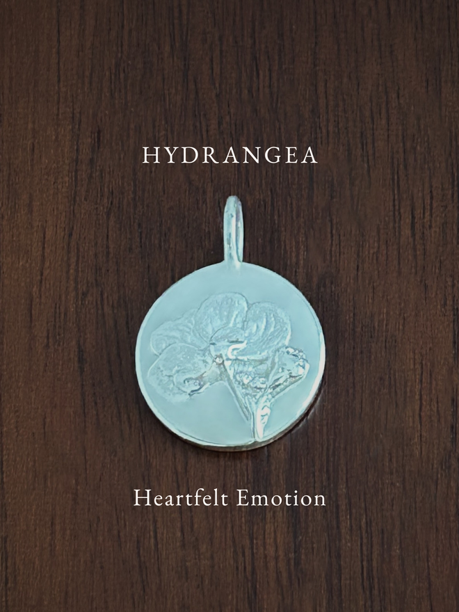 Sterling Silver Hydrangea Coin Charm on a dark background with the language of flowers meaning, heartfelt emotion