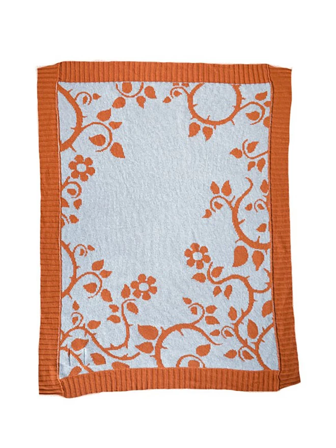 Product shot of the reverse of the rust briar rose baby blanket, muted blue background with trailing rose and thorn design in rust orange.