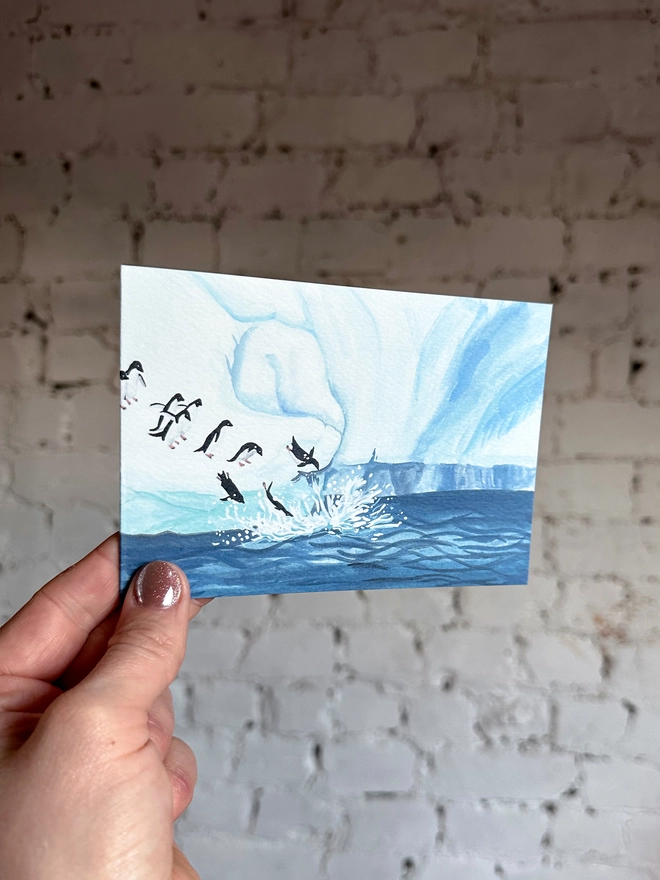  a greetings card featuring an illustration of an icy landscape with penguins diving into the sea