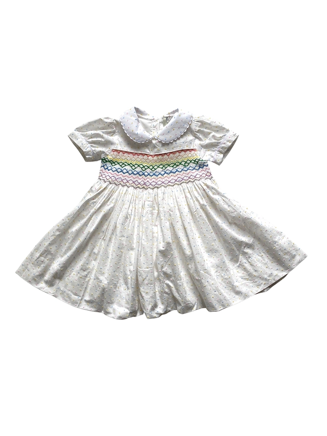 A white dress with multicoloured pastel swiss dots, a peter pan collar and rainbow smocking.