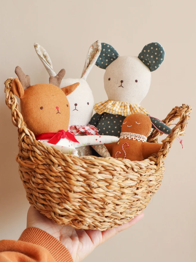 Handmade mouse doll with teal fabric featuring small white stars, a yellow gingham ruffle collar.  Handmade rabbit doll with light floral-patterned fabric, a red-and-white gingham ruffle collar. All in a small basket with Reindeer doll and gingerman bread ornament.