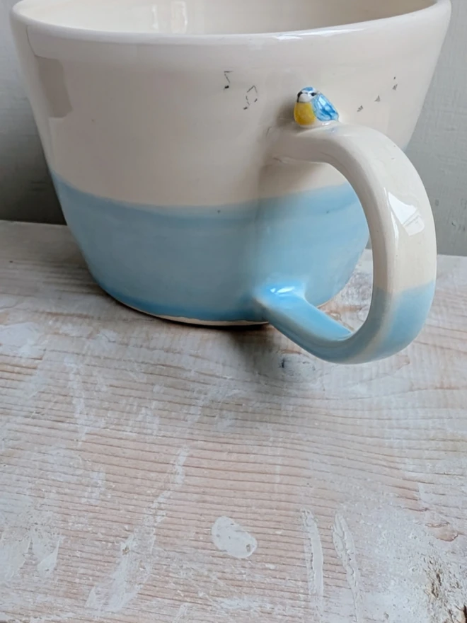 ceramic blue bird cup with a tiny bluetit bird on the handle and musical notes and bird prints on the mug