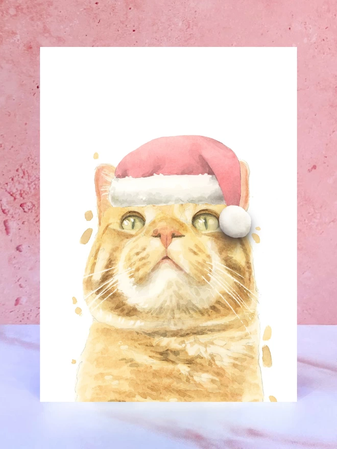 A Christmas card featuring a hand painted design of a ginger tabby cat, stood upright on a marble surface. 