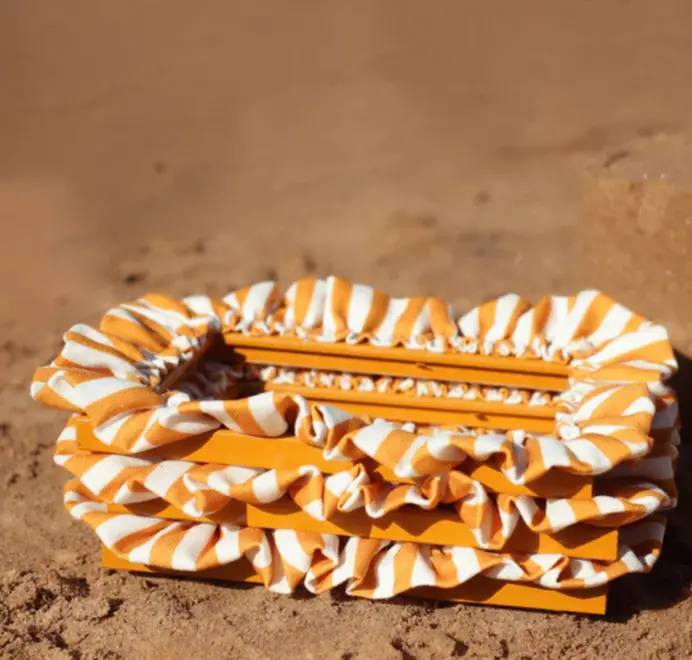 Multiple soft ruffled frames with mustard-and-white striped fabric trim stacked on top of each other on the sand.