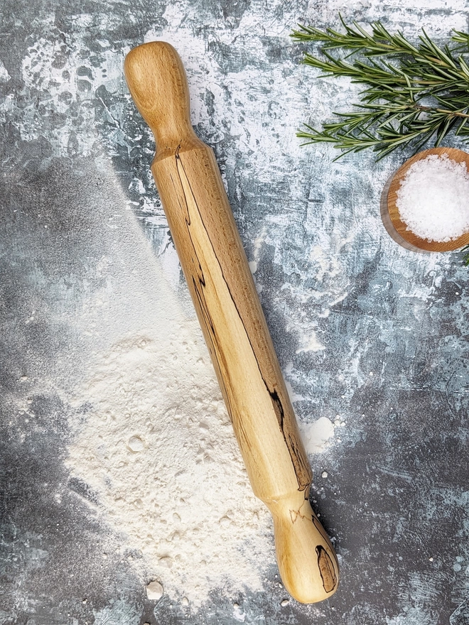 A stunning hand made rolling pin in Spalted Beech by Something From The Turnery. The rolling pin sits on an art house kitchen top amongst flour, rosemary and a wooden salt pot, prepped to bake some delicious bread!