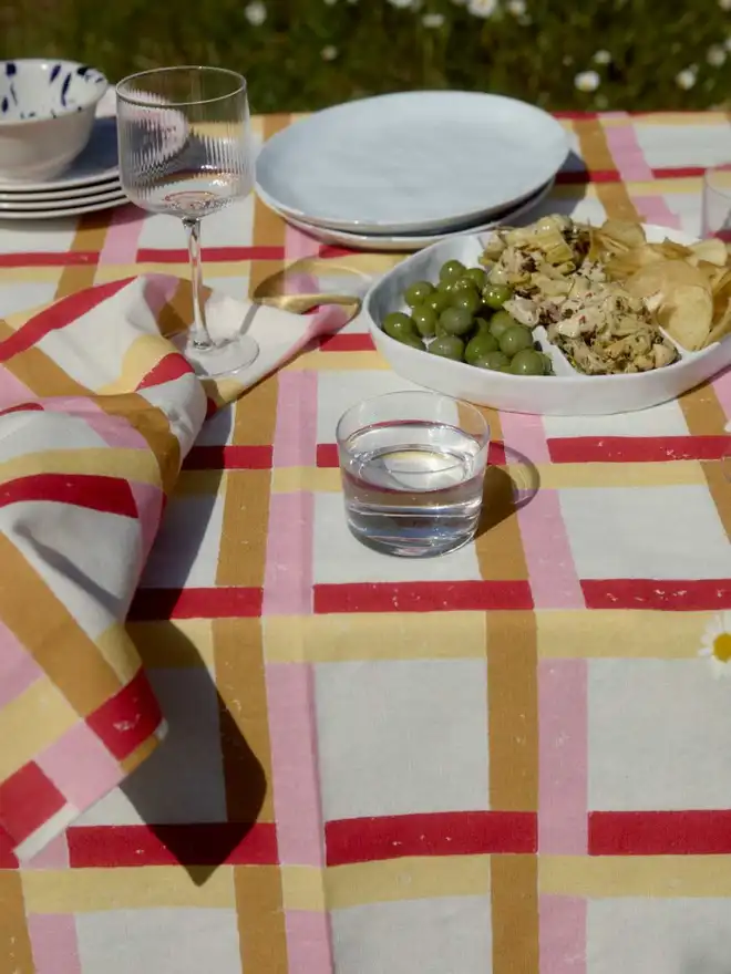 Red, sand, pink and yellow gingham tablecloth with glasses and plates