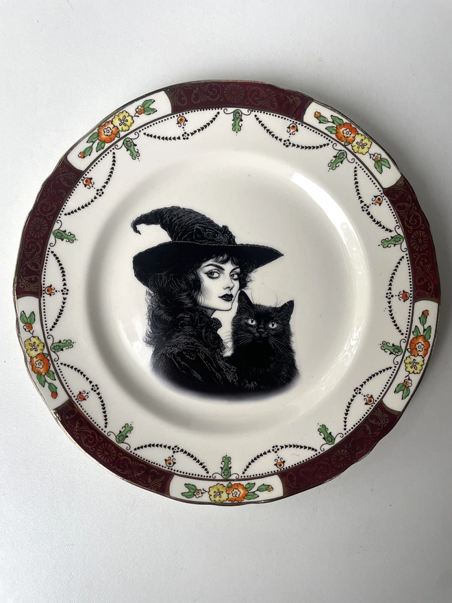 vintage plate with an ornate border, with a printed vintage illustration of a Victorian witch and her black cat in the middle