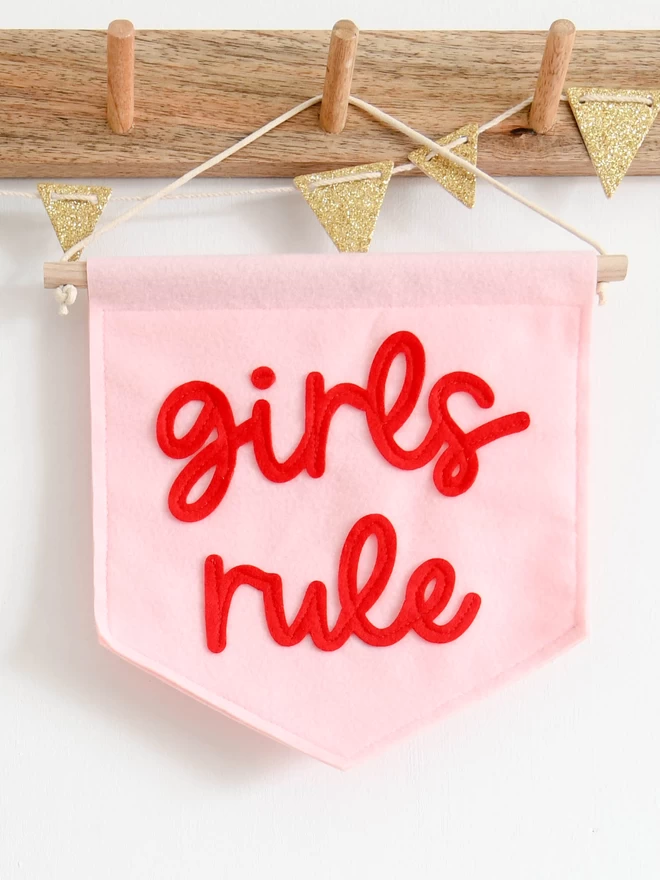 baby pink banner with girls rule sewn on in red cursive font.