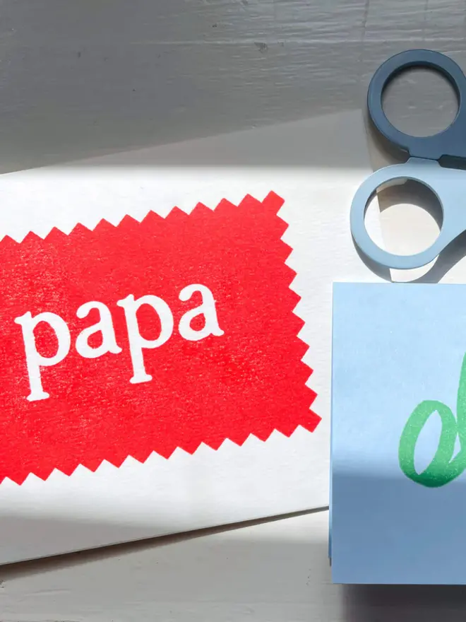 Hand-printed “Papa” card featuring cream lettering on a green zigzag-edged panel, set against a red background.