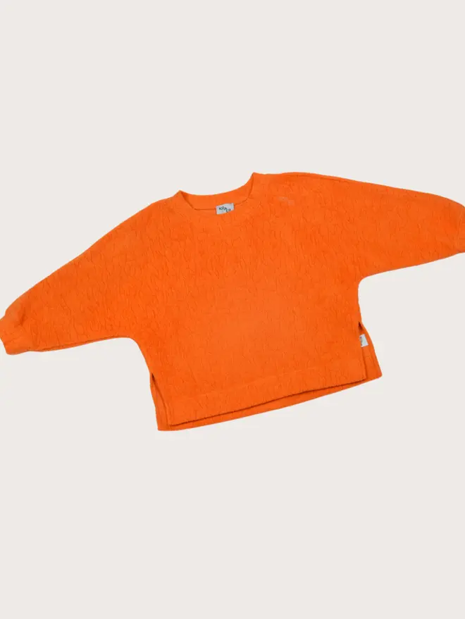 Flat lay of the Studio Koter Riverson top in Teddy Orange, a textured fleece crew neck with dropped shoulders and side splits.