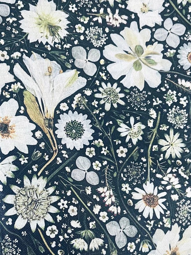 Close up of cotton tea towel with a floral design of white flowers on a black background. Flowers include Anemone, Nigella, Daisy, Astrantia, Heather, Hydrangea and Queen Anne’s Lace.