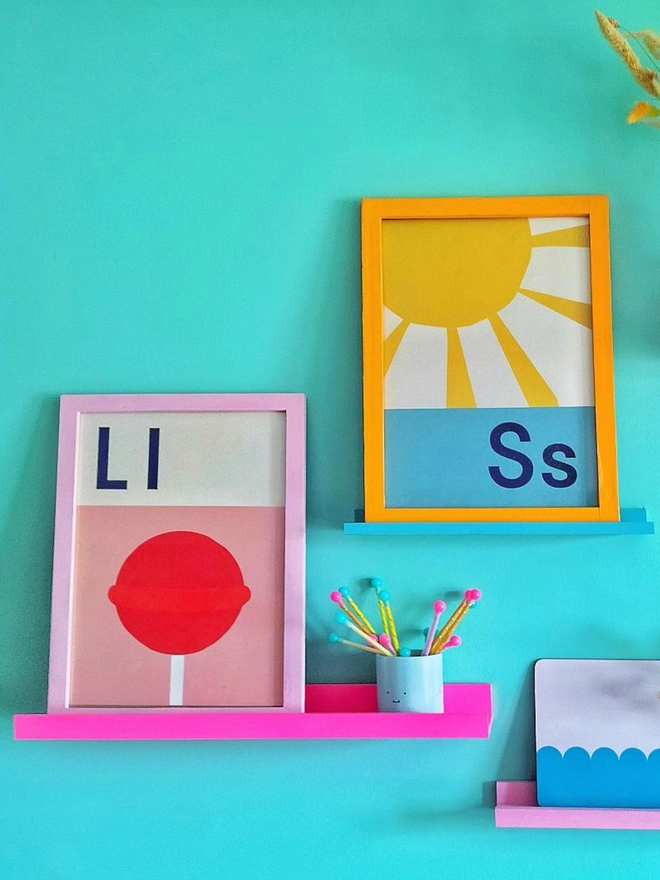 framed illustrated sunshine wall print and Lollipop print hanging on a turquoise wall