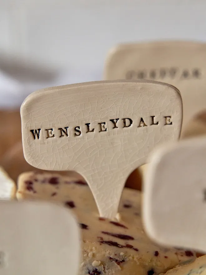 Ceramic cheese marker. That reads Wensleydale  placed on a wooden tray