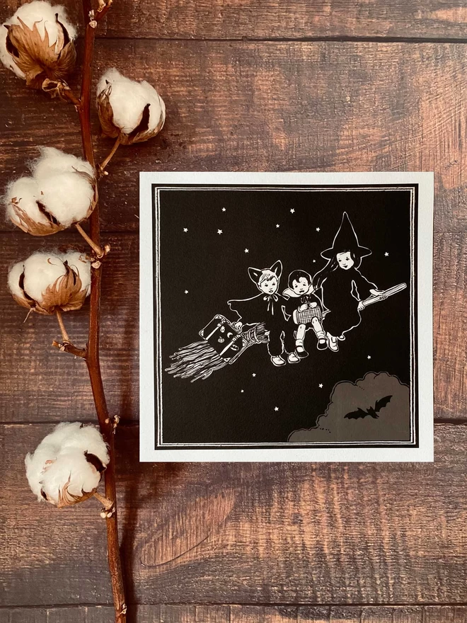 a halloween print displayed on a wooden desk with a cotton flower laid next to it