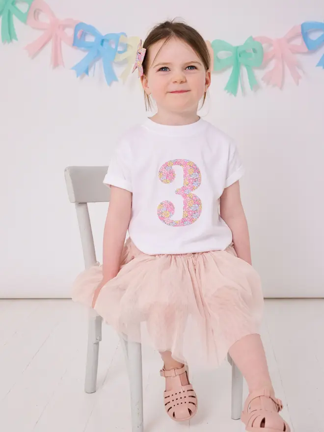 a 3 year old girl wearing a white birthday t-shirt with a number 3 cut from liberty floral print on the front