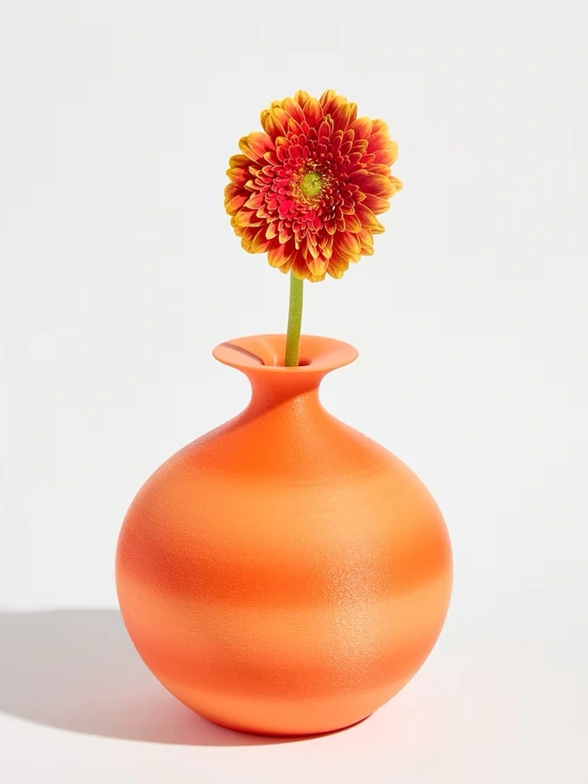 round shaped bright orange 3d printed vase holding orange flower