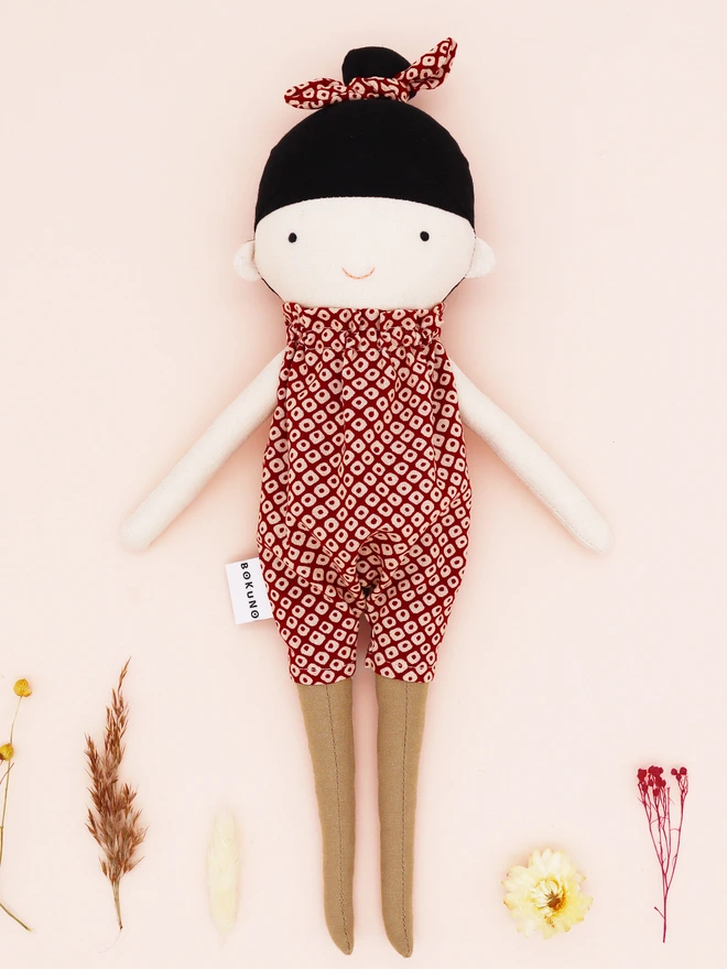 A handmade doll wearing a red and white Japanese shibori patterned jumpsuit with a matching bow in her black hair. 
