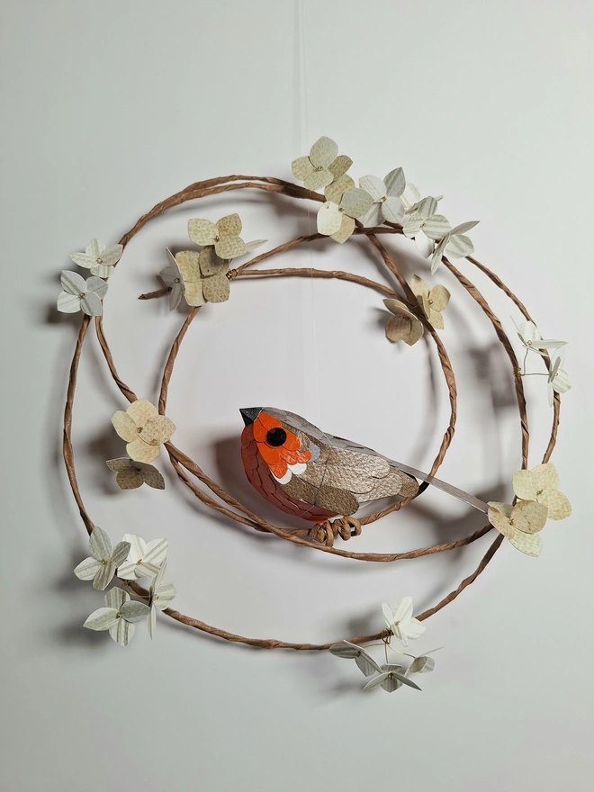 a paper sculpture depicting a robin, perched on a floral wreath of green hydrangea