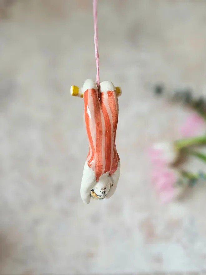 female acrobat hanging upside down in a red and pink stripe suit, hanging front view