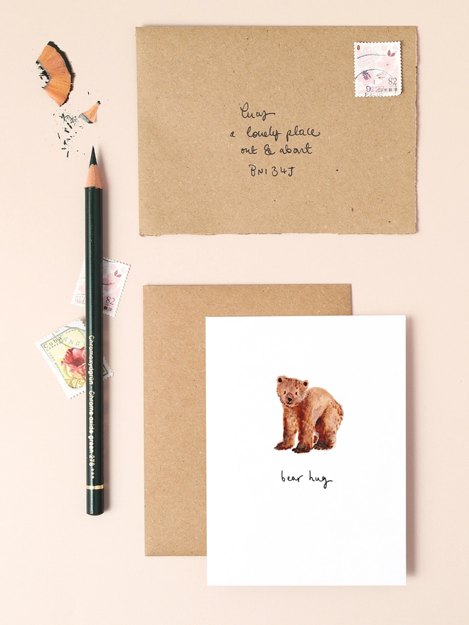 An image of a mini, rectangular white greetings card with an illustration of a brown bear. A hand written 'bear hug' message is seen under the central illustration.