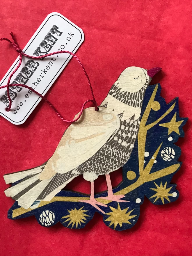 Illustrated peace dove standing on a gold star-spangled twig on a blue backroung. The cut-out decoratiojn rests on a red background