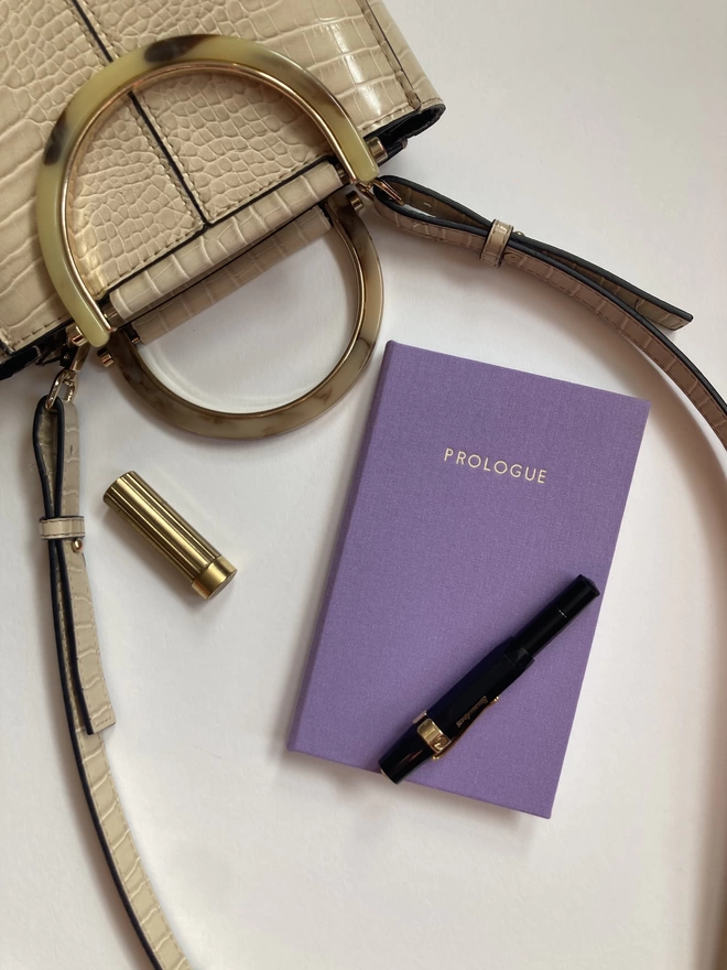 Handmade pocket sized notebook bound in Crocus cloth displayed with a small handbag and fountain pen