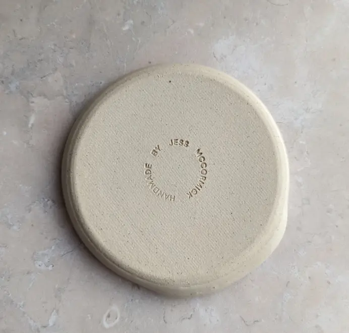 Croissant stoneware spoon rest in vanilla bean glaze against a grey marble background.