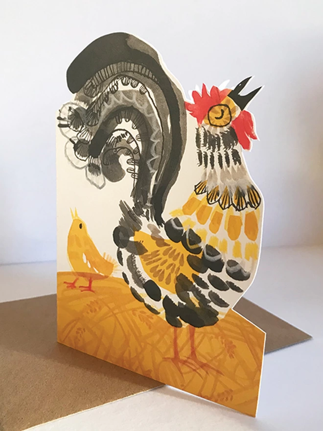 Shaped Crowing Cockerel greetings card illustrated by Esther Kent in in yellow and black, stands against a white backgroundkerel greetings card decorated in yellow and black, stands against a white background