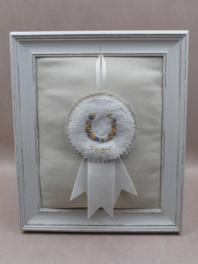 White and Beige felt rosette with embroidered Horseshoe as the central design.  Pinned to a padded frame.