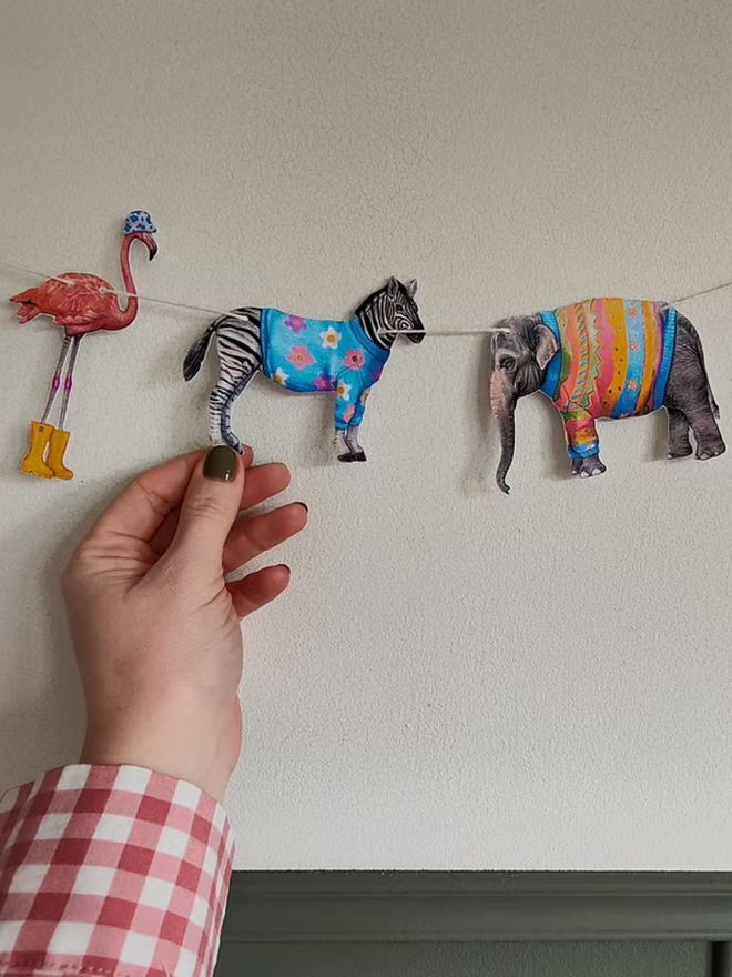 safari animals paper garland. bunting featuring illustrated animals in party outfits hung on a wall.