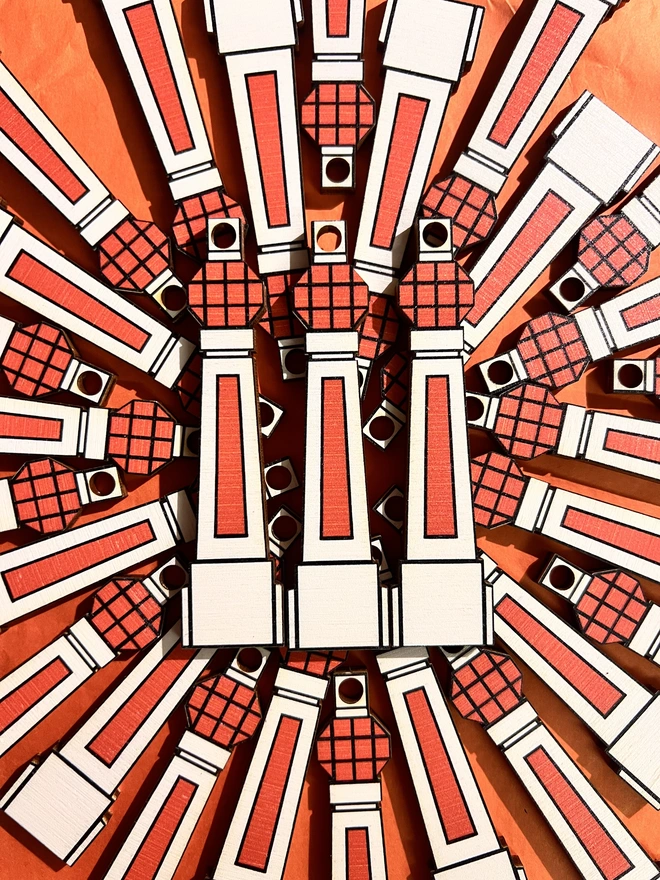 Small white and orange wooden tree decoration in the shape of Margate Lido sign. There are lots of them arranged in a patten in a flat lay on an orange card background.