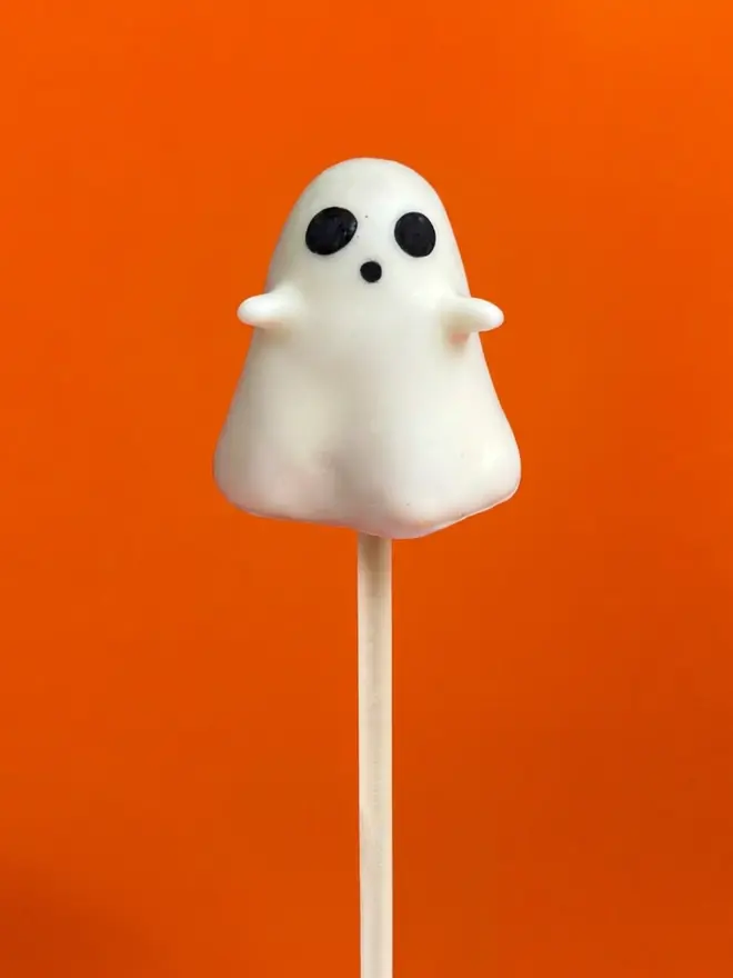 White ghost cake pop on a white stick against a bright orange background