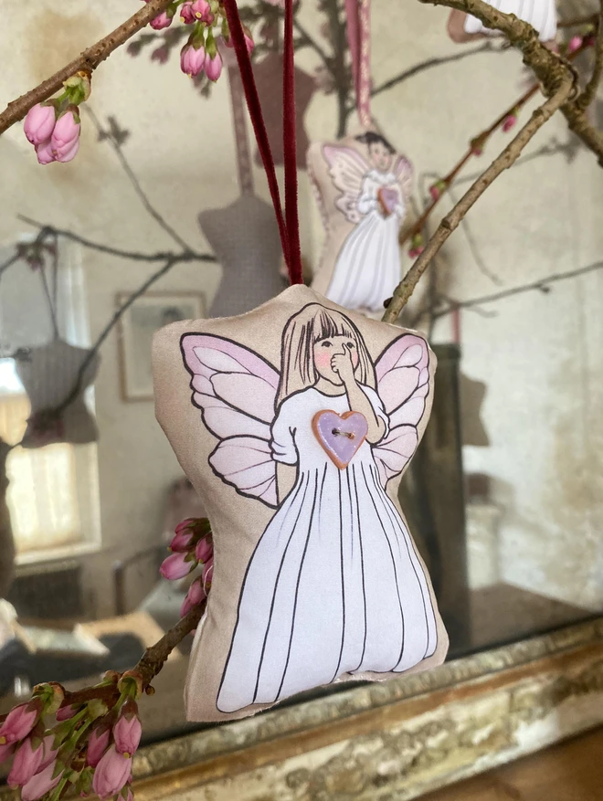 a lavender hanging fairy decoration fairy is sucking her thumb she has long fair hair and a white dress and a pottery lilac heart button sewn on her front