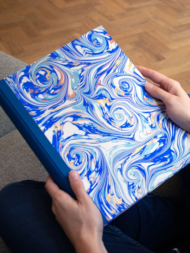 A seated person holding a photo album with blue swirly marbled paper