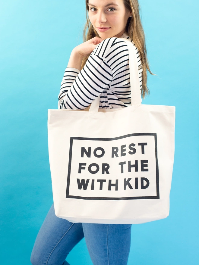a model holding a large natural canvas tote bag bearing the words no rest for the with kid