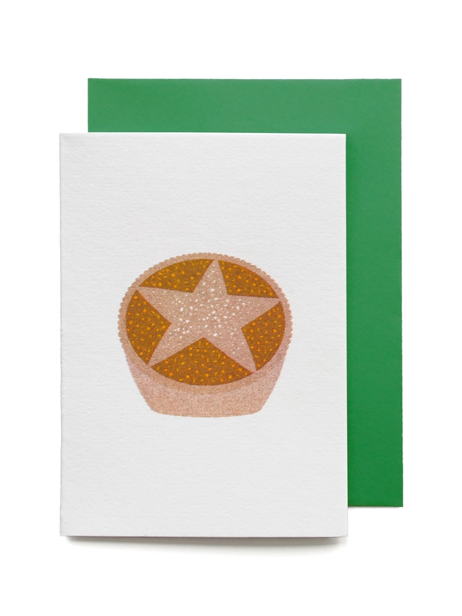 A little printed Christmas card on a white background with a festive green envelope is risograph printed with a cheekily cute Christmas mince pie
