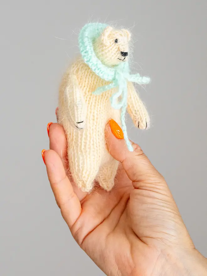 Ottilie The Bear Cashmere Figure , a cashmere bear held by a person against a grey backdrop. 