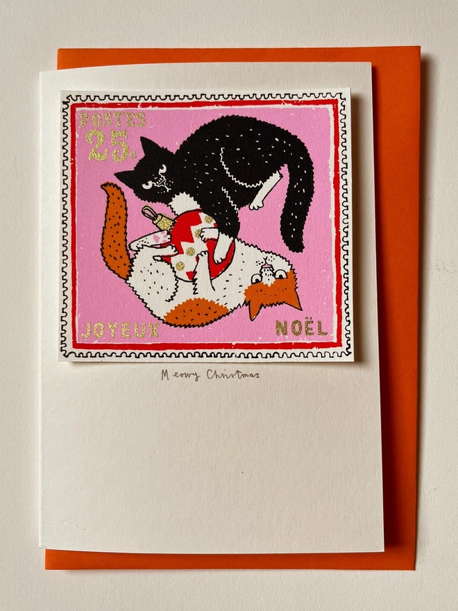 Happy Christmas Kittens Card, a white Christmas card with a colourful cat design in the centre. It is placed on an orange envelope on a white backdrop. 