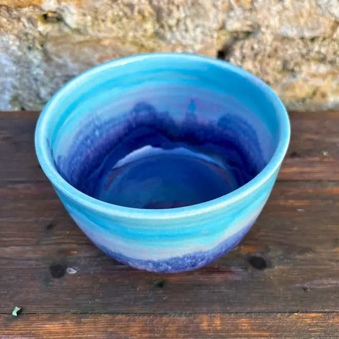 Landscape Small Bowl, a colourful bowl sitting on a wooden surface against a brick backdrop. 