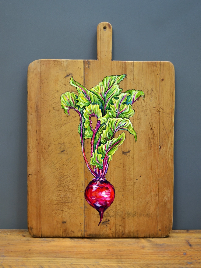 Wooden chopping board with handpainted design of a beetroot standing against a wall