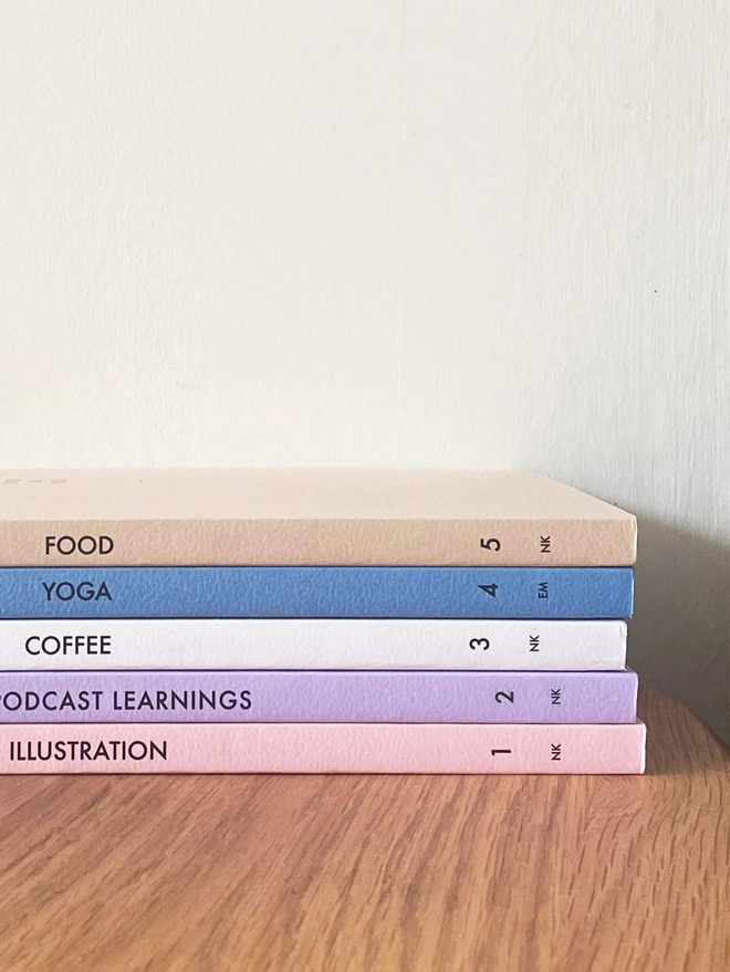 a stack of notebooks in a gradient of colours with personalised text on the spine